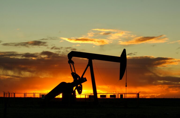 Dramatic silhouette of an oil pump jack against a vibrant sunset sky, emphasizing energy extraction.